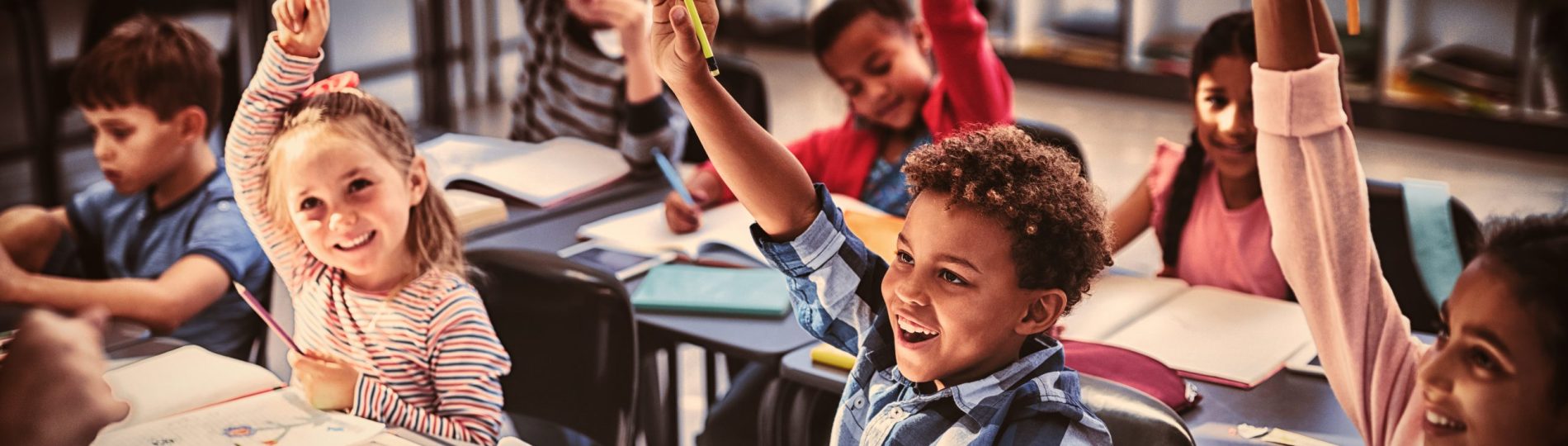 Schoolkids raising their hands in classroom In einem lebhaften Klassenzimmer in einer christlichen Schule sitzt eine Gruppe junger Kinder eifrig an ihren Tischen und hebt eifrig die Hände, um Fragen zu beantworten. Mit lächelnden Gesichtern und aufgeschlagenen Büchern verkörpern sie die Freude am Lernen in dieser förderlichen Umgebung.