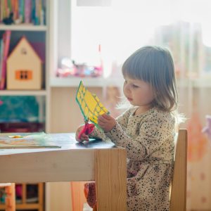 pexels-natalie-3913426 Ein kleines Kind sitzt an einem Tisch in einem Spielzimmer, das möglicherweise zu einer christlichen Schule gehört, und ist ganz auf ein Bastelprojekt mit buntem Papier konzentriert. In dem gut beleuchteten Raum stehen Regale mit Spielzeug und Büchern, und im Hintergrund ist eine kleine Staffelei zu sehen.