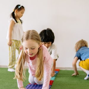 pexels-yan-krukov-8613318 Vier Kinder spielen auf einem grünen Teppich mit bunten, strukturierten Matten in der Danielschule. Ein Mädchen mit Zöpfen im Vordergrund krabbelt vor sich hin, gefolgt von einem Jungen. Zwei andere Kinder stehen und hocken in der Nähe, alle spielen in dieser lebendigen christlichen Schule.
